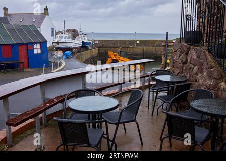 Auf dem nassen und leeren Café-Tisch bietet sich ein Blick auf den Hafen von St. Abbs mit Fischerbooten, die für Wartungsarbeiten an der Hafenmauer aufgestellt wurden Stockfoto