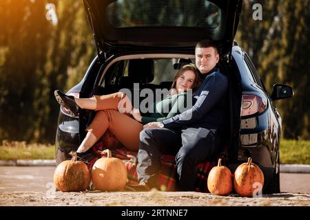 Ein verliebtes Paar sitzt und umarmt sich am Herbsttag im Kofferraum des Parkhauses mit Kürbissen. Positives und romantisches Mann-und-Frau-fest Stockfoto