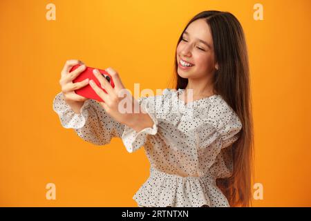 Teen Mädchen macht ein Selfie auf ihrem Handy vor gelbem Hintergrund Stockfoto