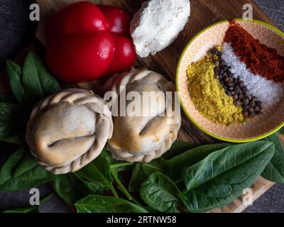 Die frischen Empanadas werden auf einem Holzbrett mit einer Schüssel mit Gewürzen und Kräutern serviert Stockfoto