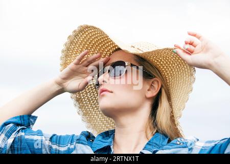 Junge Dame, die in die Ferne schaut, mit Sonnenbrille und Sonnenhut Stockfoto
