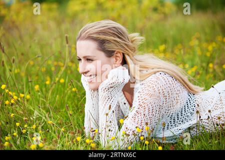 Junge Dame lächelt, während sie vorne auf einem Feld liegt Stockfoto