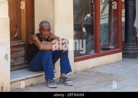 Havanna, Kuba - 30. August 2023: Ein kubanischer Afroamerikaner sitzt vor der Haustür eines Gebäudes. Stockfoto