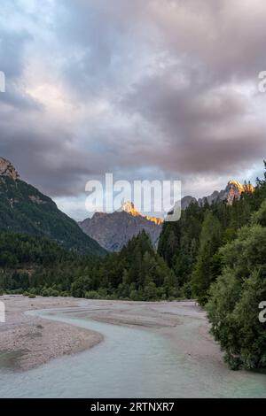 Die untergehende Sonne trifft auf den Gipfel des Berges über einem gletschblauen Fluss in den alpen in Slowenien Stockfoto