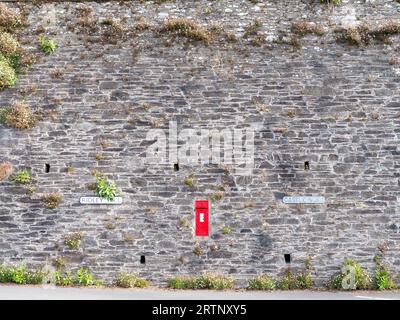 Ein roter Postkasten in der Mitte einer großen Steinmauer in einem Dorf in England Stockfoto