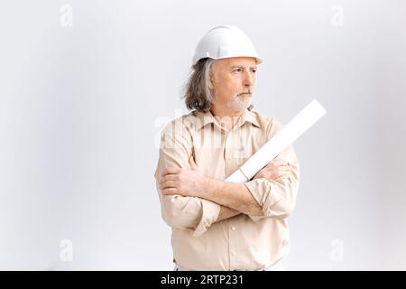 Professioneller weißer, grauhaariger Mann mittleren Alters, Vorarbeiter, Architekt Bauarbeiter in weißem Schutzhelm, der einen Architekturplan auf dem Gebäude hält, schaut zur Seite, steht auf isoliertem weißem Hintergrund Stockfoto