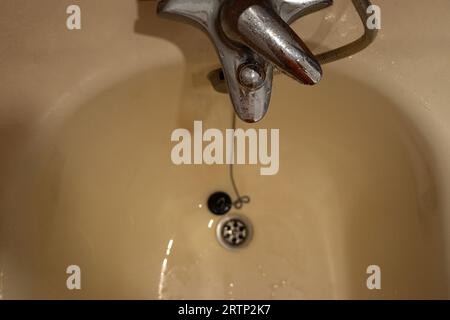 Abfluss und Wasserhahn mit Dusche in einem alten schmutzigen Bad in einem Appartement in der Nähe Stockfoto