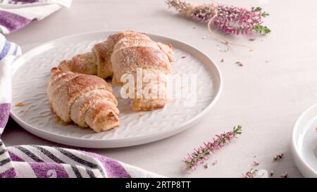 Kleine Croissants auf weißen Keramikplatten, hausgemachte Kuchen auf Betontischplatte. Stockfoto