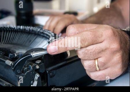 Nahaufnahme der männlichen Hand, die den Wagenrückstellhebel an einer schwarzen Vintage-Schreibmaschine betätigt. Stockfoto