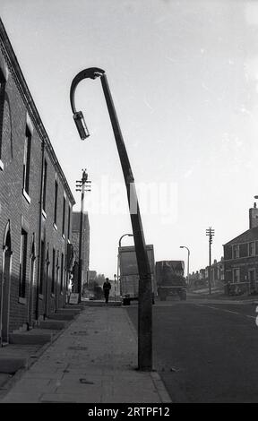 1960er Jahre, historisch, ein geknickter Laternenpfahl in der Straße mit kleinen viktorianischen Reihenhäusern, Ripponden Rd, Oldham, England, Großbritannien. Gegenüber einem Wilson's Pub, dem Bulls Head. Stockfoto