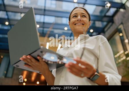 Nahaufnahme einer stilvollen Geschäftsfrau, die auf einem Laptop arbeitet und auf einem modernen Bürohintergrund steht Stockfoto