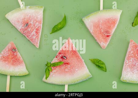 Gefrorene Wassermelonen-Eiskraut auf trendigem Savannah-grünem Hintergrund. Erfrischendes Dessert im Sommer, flach gelegen, Blick von oben Stockfoto