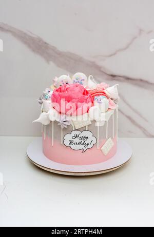 Wunderschöner und eleganter grau-rosa Kuchen mit geschmolzener weißer Schokolade, Makronen, essbarer Pfingstrosenblüte und Meringue-Küssen Stockfoto
