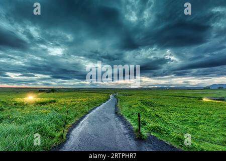 Dramatischer Blick auf den Weg auf dem landwirtschaftlichen Feld und stimmungsvoller Himmel im Sommer auf Island Stockfoto