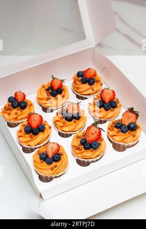 Orange Cupcakes mit frischen Beeren und Buttercreme in der Geschenkbox Stockfoto