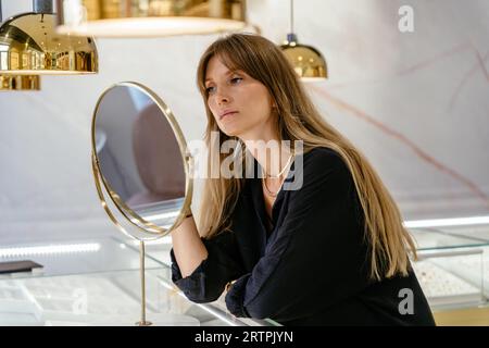 Schöne langhaarige kaukasische Frau, die Schmuck in einem modernen Juweliergeschäft aussucht. Stockfoto