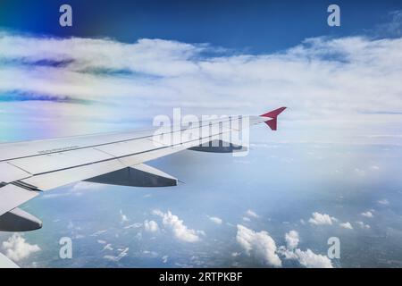 Allgemeine Ansicht eines Flugzeugflügels, der über eine Landschaft fliegt und durch die Wolken hindurch gesehen werden kann. Stockfoto