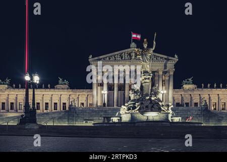 Wien, Österreich. Blick auf das Wiener parlamentsgebäude, das nachts beleuchtet wird, mit der schwenkenden österreichischen Flagge und dem Pallas-athene-Brunnen im Stockfoto