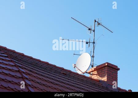 Passive analoge und Satelliten-TV-Anetennas auf dem Dach, die am Schornstein gegen den blauen Himmel befestigt sind Stockfoto