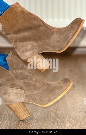 Nahaufnahme. Wildlederstiefel für Damen. Braune Damenschuhe. Beim Mädchen werden warme Stiefel auf die Beine gestellt. Schuhanpassung.Konzept des Kaufens, des Versuchs an Schuhen und Stiefeln. Stockfoto