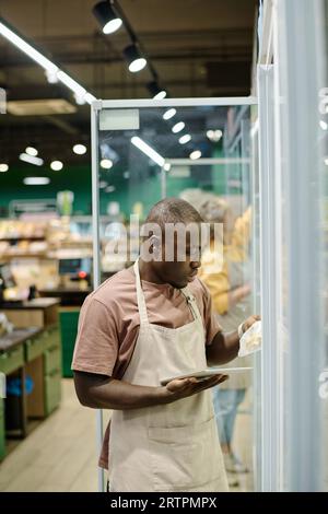 Afroamerikanischer Mitarbeiter des Geschäfts, der die Haltbarkeit von Waren mit Tablet-pc im Supermarkt überprüft Stockfoto