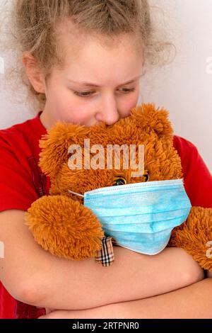 Ein Mädchen hält einen Spielzeugbären. Das Kind hat einen Bären in einer Maske. Das Konzept der Pflege für Angehörige, Kinder in Quarantäne. Virenschutz, Prävention epid Stockfoto