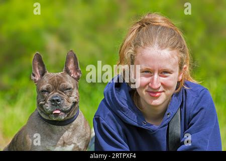 Mädchen posiert mit Lilac Französisch Bulldog / Isabella frenchie / Bouledogue Französisch, Rasse von Französisch Begleithund oder Spielzeug Hund im Garten Stockfoto