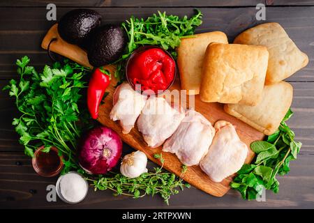 Chimichurri Chicken Sandwich Zutaten auf einem Holztisch: Rohe Hähnchenschenkel, Ciabatta Brot und andere ungekochte Sandwich-Zutaten Stockfoto
