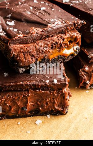 Karamell-Schokoladen-Käsekuchen-Dessertstangen mit Ganache-Belag: Schichten von Schokoladenkruste, Karamell, Käsekuchenfüllung und dunkler Schokoladenganache Stockfoto