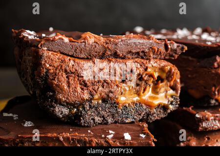 Karamell-Schokoladen-Käsekuchen-Dessertstangen mit Ganache-Belag: Schichten von Schokoladenkruste, Karamell, Käsekuchenfüllung und dunkler Schokoladenganache Stockfoto