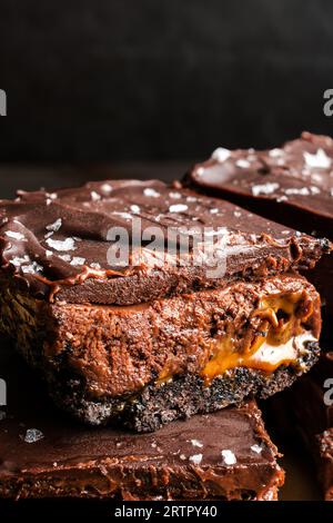 Karamell-Schokoladen-Käsekuchen-Dessertstangen mit Ganache-Belag: Schichten von Schokoladenkruste, Karamell, Käsekuchenfüllung und dunkler Schokoladenganache Stockfoto