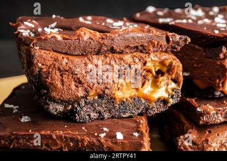 Karamell-Schokoladen-Käsekuchen-Dessertstangen mit Ganache-Belag: Schichten von Schokoladenkruste, Karamell, Käsekuchenfüllung und dunkler Schokoladenganache Stockfoto