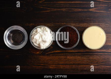 Vietnamesischer Joghurt-Kaffee (Sua Chua Cafe) Zutaten: Gemahlener Kaffee, gesüßter Joghurt, Kondensmilch und Wasser auf einem Holztisch Stockfoto