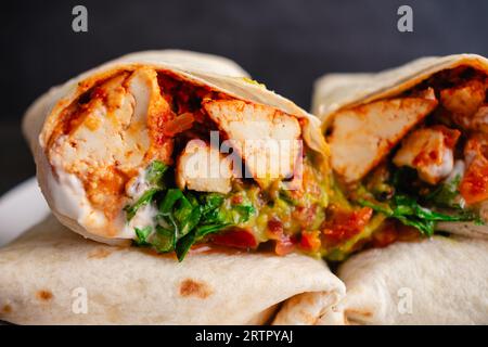 Nahansicht eines in zwei Hälften geschnittenen Sofritas Burrito: Scharfer Tofu-Burrito gefüllt mit Guacamole, veganer Sauerrahm, Koriander, Salat, Salsa, und Tomaten Stockfoto