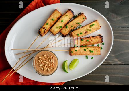 Veganer Tofu Satay mit Erdnusssauce: Marinierter Tofu auf Bambusspießen mit Erdnusssauce und Limettenspießen Stockfoto