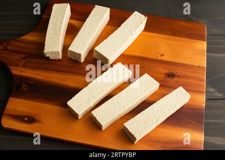 Tofu-Scheiben auf einem Holzschneidebrett: Gepresste und in Scheiben geschnittene lange rechteckige Stücke Bohnenquark Stockfoto