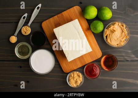 Tofu Satay mit Erdnusssauce Zutaten auf einem Holztisch: Bohnenquark, umgeben von Limetten, Erdnussbutter und anderen Zutaten für eine vegane Vorspeise Stockfoto