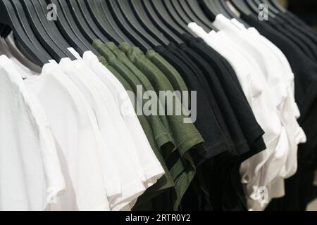 Eine Kollektion pastellfarbener T-Shirts, die auf einem Kleiderständer auf einer Theke in einem Geschäft hängen. Selektives Schärfen, Hintergrund. Stockfoto