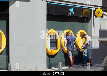 Viladecans, Spanien - 14. September 2023: Zwei Mann und ein Kind vor dem Geldautomaten Caixa ziehen an einem sonnigen Tag Geld ab. Stockfoto