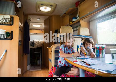 Zwei kaukasische Kinder, Bruder und Schwester, die während einer Autotour in einen Wohnwagen ziehen. Campingurlaub mit Kindern im Hintergrund Stockfoto