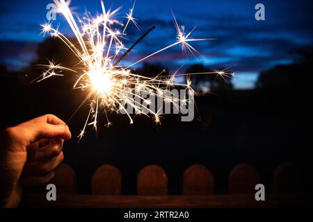 Hand hält einen Sparkler oder bengalischen Feuerstab, der in der blauen Abenddämmerung im Freien brennt. Feiertage oder magischer Hintergrund oder Hintergrund. Stockfoto