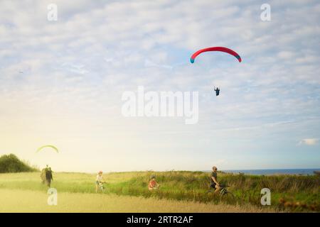 VIERVILLE SUR MER, AUGUST 2023 - der Gleitschirmflugplatz am Strand von Omaha, mit Menschen auf Fahrrädern bei Sonnenuntergang. Stockfoto