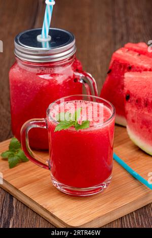 Nahaufnahme von Wassermelonensaft in einem Glasbecher mit Minzblättern vor dem Hintergrund von geschnittener Wassermelone. Leerzeichen kopieren. Stockfoto