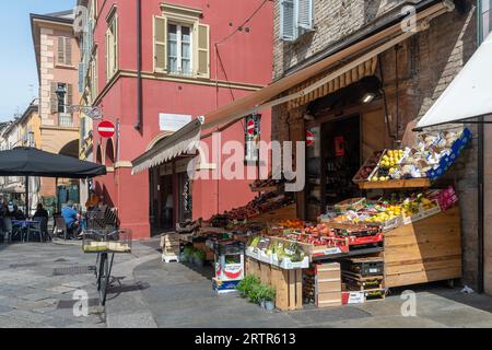 Gemüsehändler mit Obst und Gemüse auf der Straße und Menschen in einem Straßencafé in der Altstadt, Parma, Emilia-Romagna, Italien Stockfoto