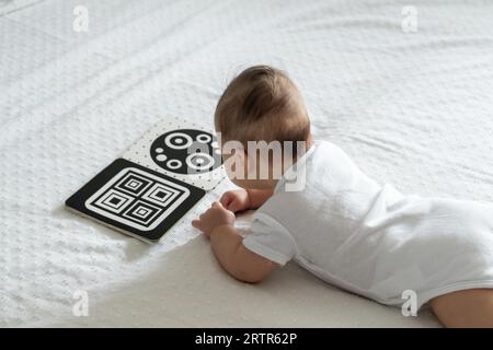 Ein Baby schaut sich ein Schulungsbuch mit Schwarz-weiß-Kontrast an. Intellektuelle Entwicklung des Neugeborenen. Karten für Kinder entwickeln. Stockfoto