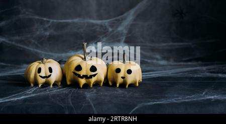 Halloween-Kürbisse in Geisterform auf dunkelgrauem Hintergrund mit Spinnweben. Halloween-Grußkarte mit Kopierplatz. Jacks Haupthintergrund. Stockfoto