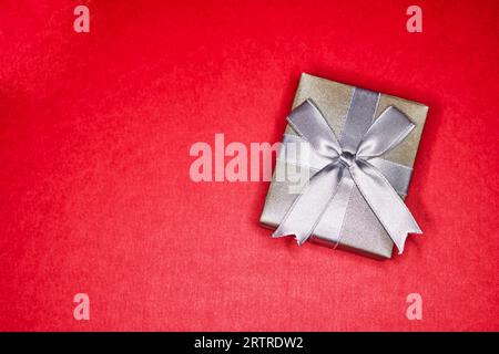 Silberne Geschenkbox mit Band und Schleife isoliert auf Rot Stockfoto