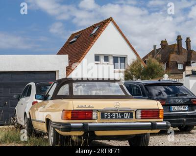 Neufchatel-Hardelot, Frankreich - 18. August 2023: Ein Mercedes-Benz 380 SL im Oldtimer-Stil parkte elegant vor einem Haus, flankiert von einem Audi-Wagen und einem kompakten Fiat-Miniauto. Stockfoto