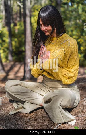 Die Frau meditiert mit den Händen, die im Wald eingeschlossen sind. Vertikale Aufnahme Stockfoto