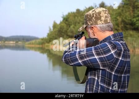 Mann mit Jagdgewehr in der Nähe des Sees im Freien. Leerzeichen für Text Stockfoto